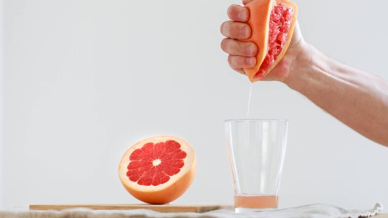 Mann presst halbe Grapefruit aus der Hand in ein Glas.