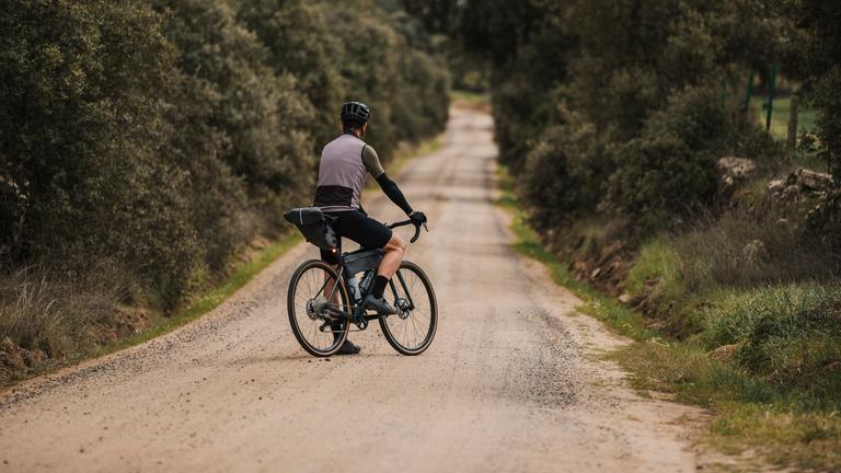Ein Fahrradfahrer steht mit dem Gravelbike auf einer Landstraße in Spanien.