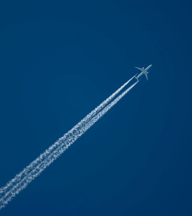 Ein Verkehrsflugzeug zieht am Himmel Kondensstreifen hinter sich her.