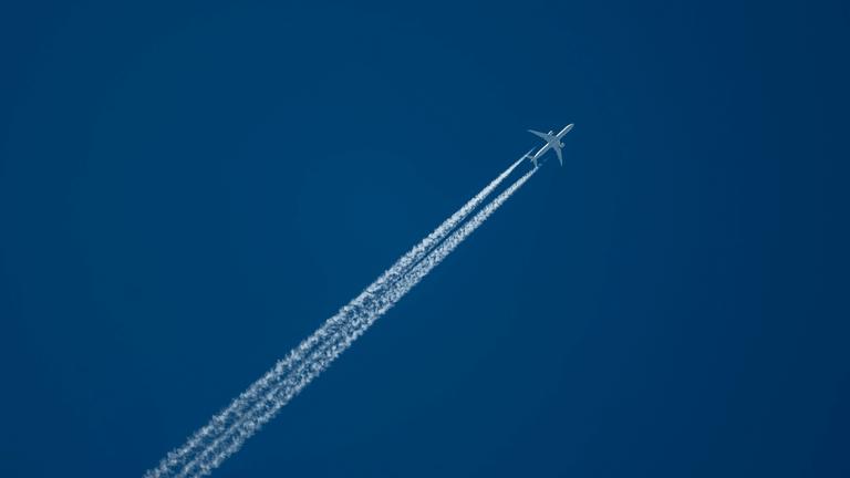 Ein Verkehrsflugzeug zieht am Himmel Kondensstreifen hinter sich her.