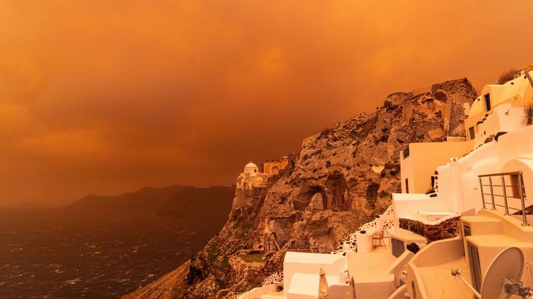 Ein kräftiger Sturm trägt Sand aus Afrika über die Insel Santorini und färbt den Himmel orangerot ein.