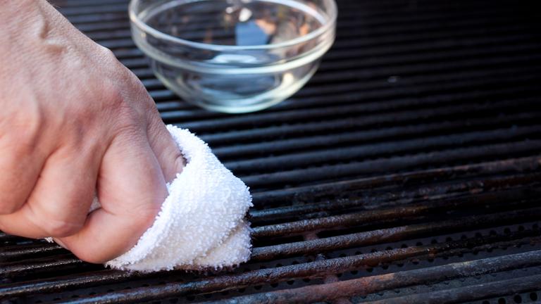 Ein Mann reinigt einen Grillrost mit einem weißem Lappen.