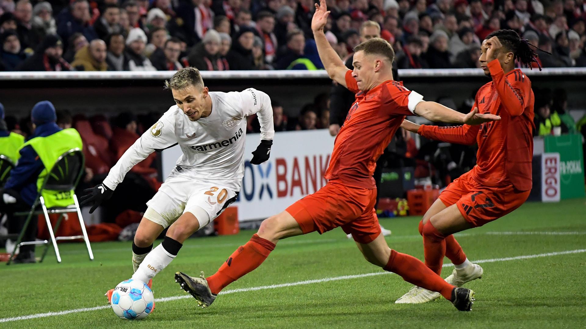 Im DFB-Pokal-Achtelfinale am 03.12.2024 geht Bayers Grimaldo gegen Bayern Kimmich und Olise in den Kampf um den Ball. 