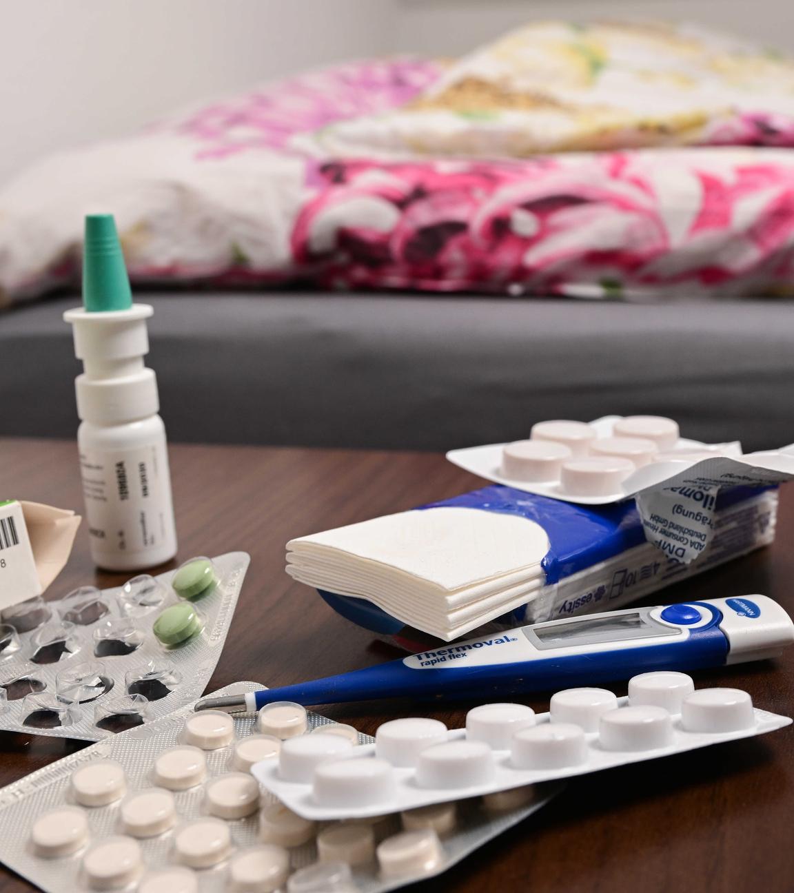 Ein Fieberthermometer und Medikamente liegen auf einem Nachttisch (gestellte Szene).