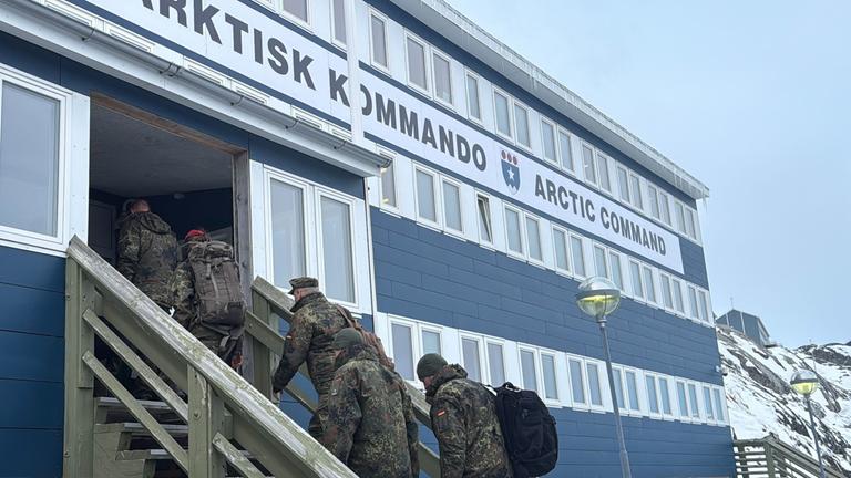 Mehrere Bundeswehr-Soldaten gehen die Treppe zu einem Gebäude mit der Aufschrift "Arktisk Kommando - Arctic Command" hinauf. Im Hintergrund schneebedeckte Berge.