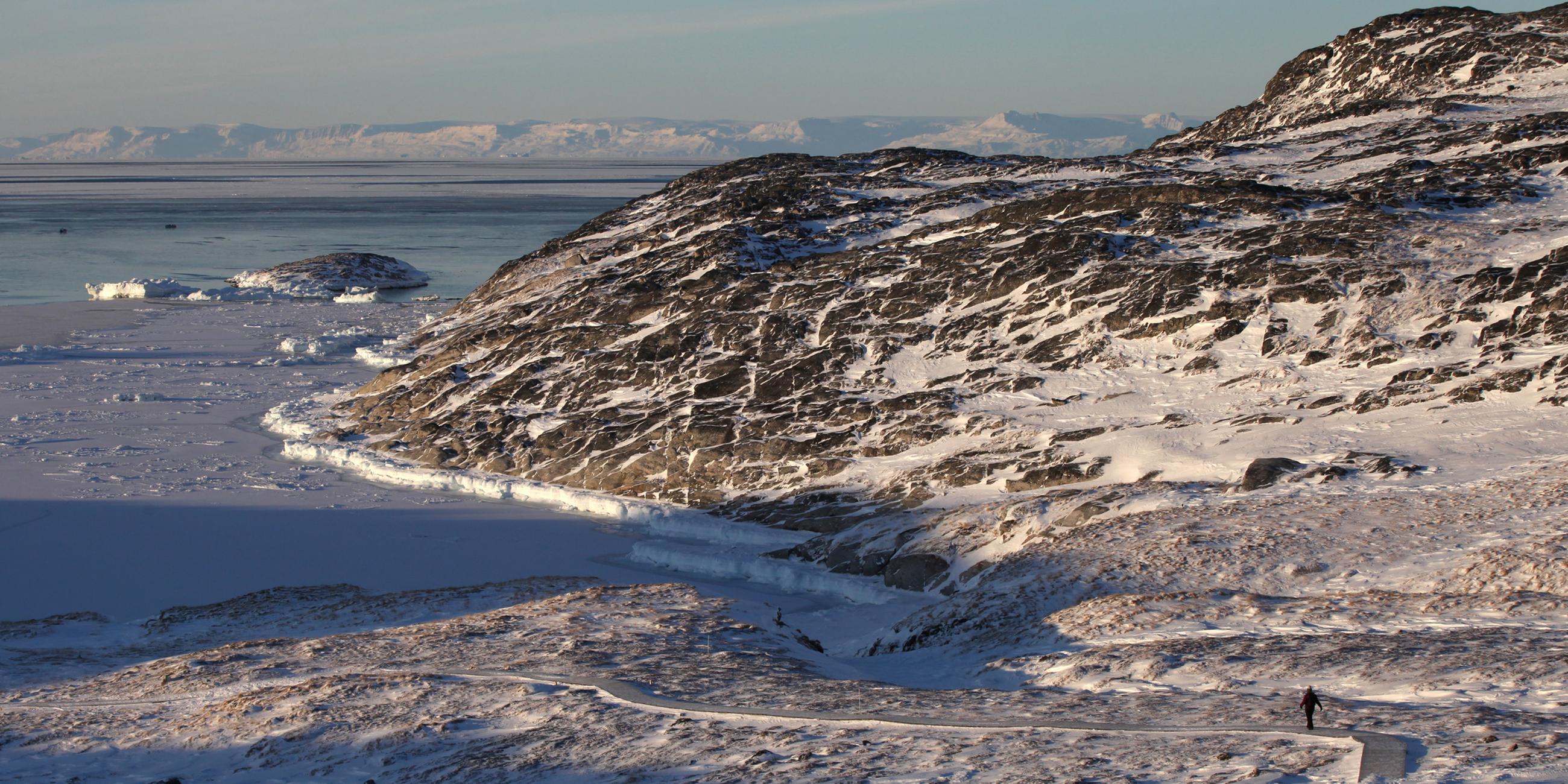 Eine Frau geht am Ilulissat-Eisfjord durch eine verschneite Gesteinslandschaft. 
