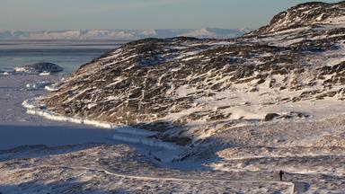 Eine Frau geht am Ilulissat-Eisfjord durch eine verschneite Gesteinslandschaft. 