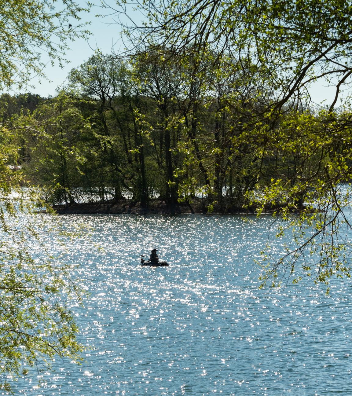 Ein Mann angelt auf dem Groß Glienicker See, dessen Wasser im Licht der Morgensonne glitzert.