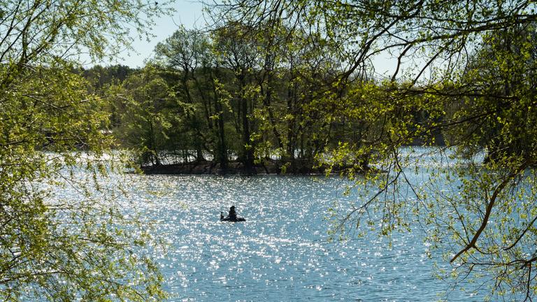 Ein Mann angelt auf dem Groß Glienicker See, dessen Wasser im Licht der Morgensonne glitzert.