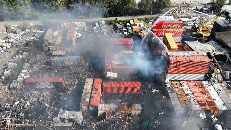 26.08.2025, Hamburg: Einsatzkräfte der Feuerwehr löschen einen Brand in einem Industriegebiet im Hamburger Hafen, in dem am Vortag ein Großbrand ausgebrochen war.