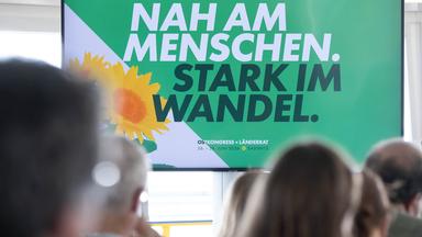 Plakat mit dem Motto "Nah am Menschen, stark im Wandel", davor sitzen Menschen.