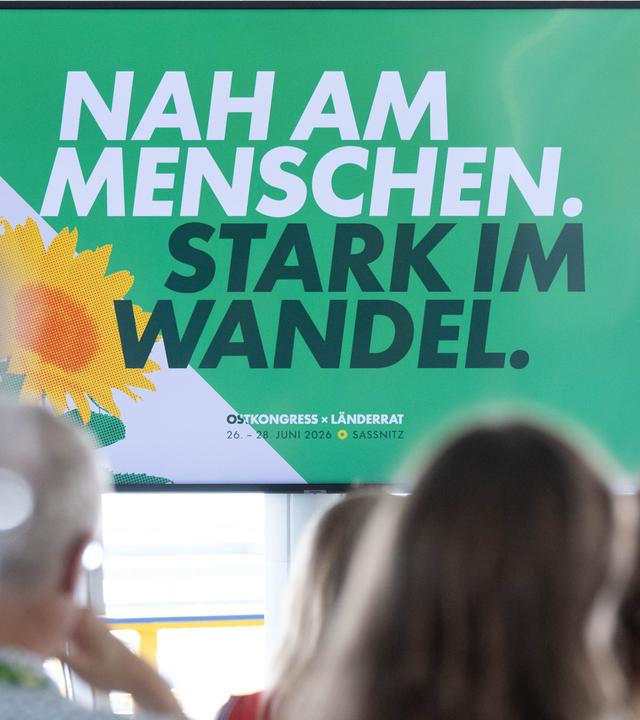 Plakat mit dem Motto "Nah am Menschen, stark im Wandel", davor sitzen Menschen.