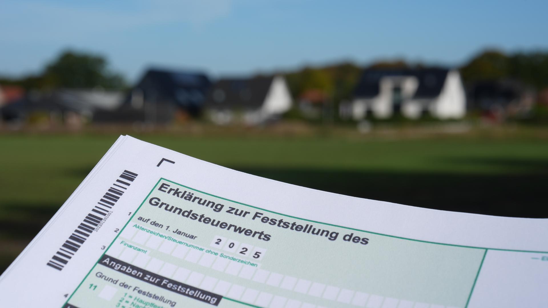 17.10.2024, Schleswig-Holstein, Jersbek: Eine Erklärung zur Feststellung des Grundsteuerwerts für das Jahr 2025 wird vor eine Wohnsiedlung hochgehalten.
