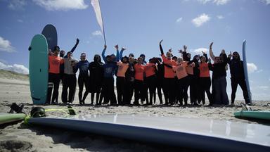 Kinder und Jugendliche des Social Surf Club stehen mit ihren Surfbrettern am Strand.