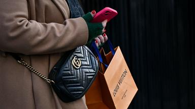 Eine Fußgängerin mit einer Gucci-Umhängetasche trägt eine Louis-Vuitton-Tüte in der Hand.
