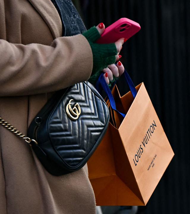 Eine Fußgängerin mit einer Gucci-Umhängetasche trägt eine Louis-Vuitton-Tüte in der Hand.