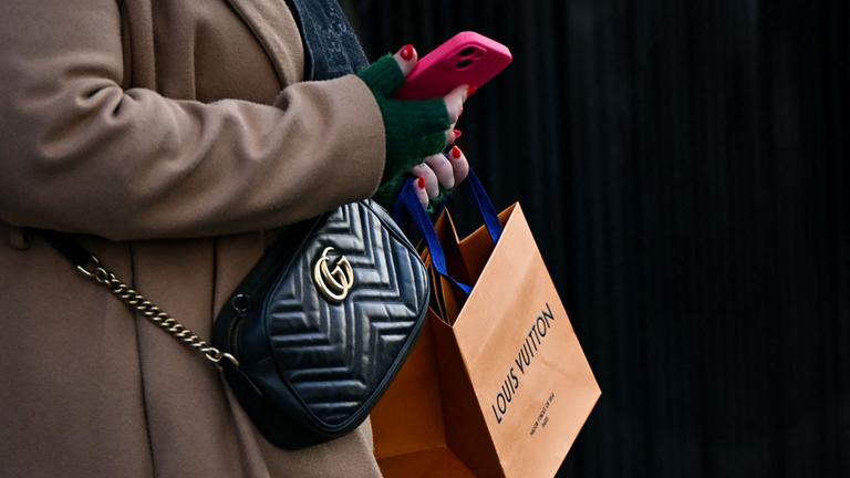 Eine Fußgängerin mit einer Gucci-Umhängetasche trägt eine Louis-Vuitton-Tüte in der Hand.