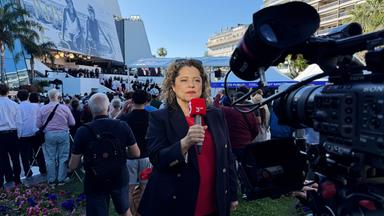 Eine Frau mit einem 3sat-Mikrofon wird von einer Kamera gefilmt, während sie vor dem Kino in Cannes steht und einen Aufsager macht.