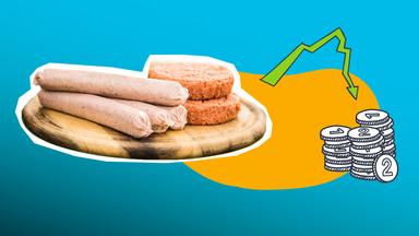 Auf dem Bild ist ein Holzbrett mit vier veganen, rohen Bratwürsten und zwei fleischlosen Burgerpatties zu sehen. Außerdem ist daneben ein kleiner Haufen Münzen und ein absteigender Pfeil in grün zu erkennen. Der Hintergrund ist orange und blau.