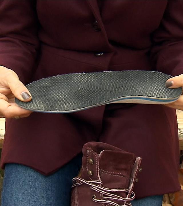 Frau sitzt auf einer Bank und hält eine Schuheinlegesohle in der Hand.