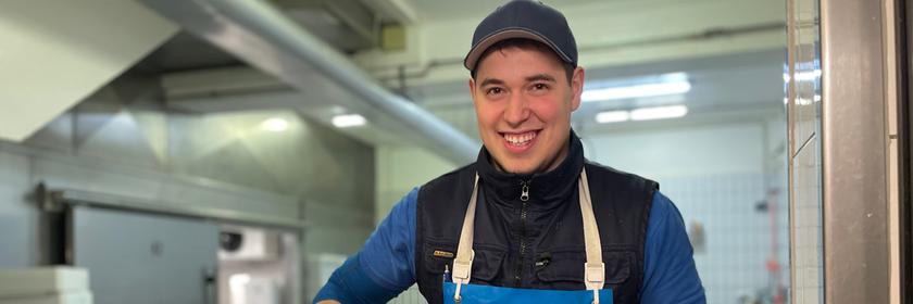 Julian bei der Arbeit, in der einen Hand hält er eine große Schaufel mit Eis. Vor ihm ist eine Plastikwanne mit ganzen Fischen.
