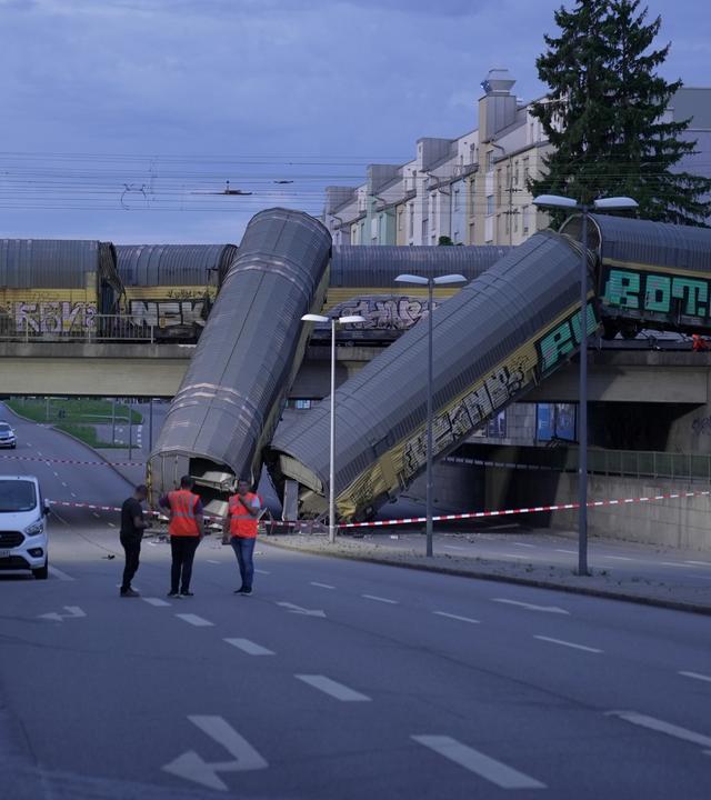 0.06.2026, Bayern, München: Zwei Waggons eines Güterzugs liegen auf einer Straße, nachdem sie von einer Brücke gestürzt sind.