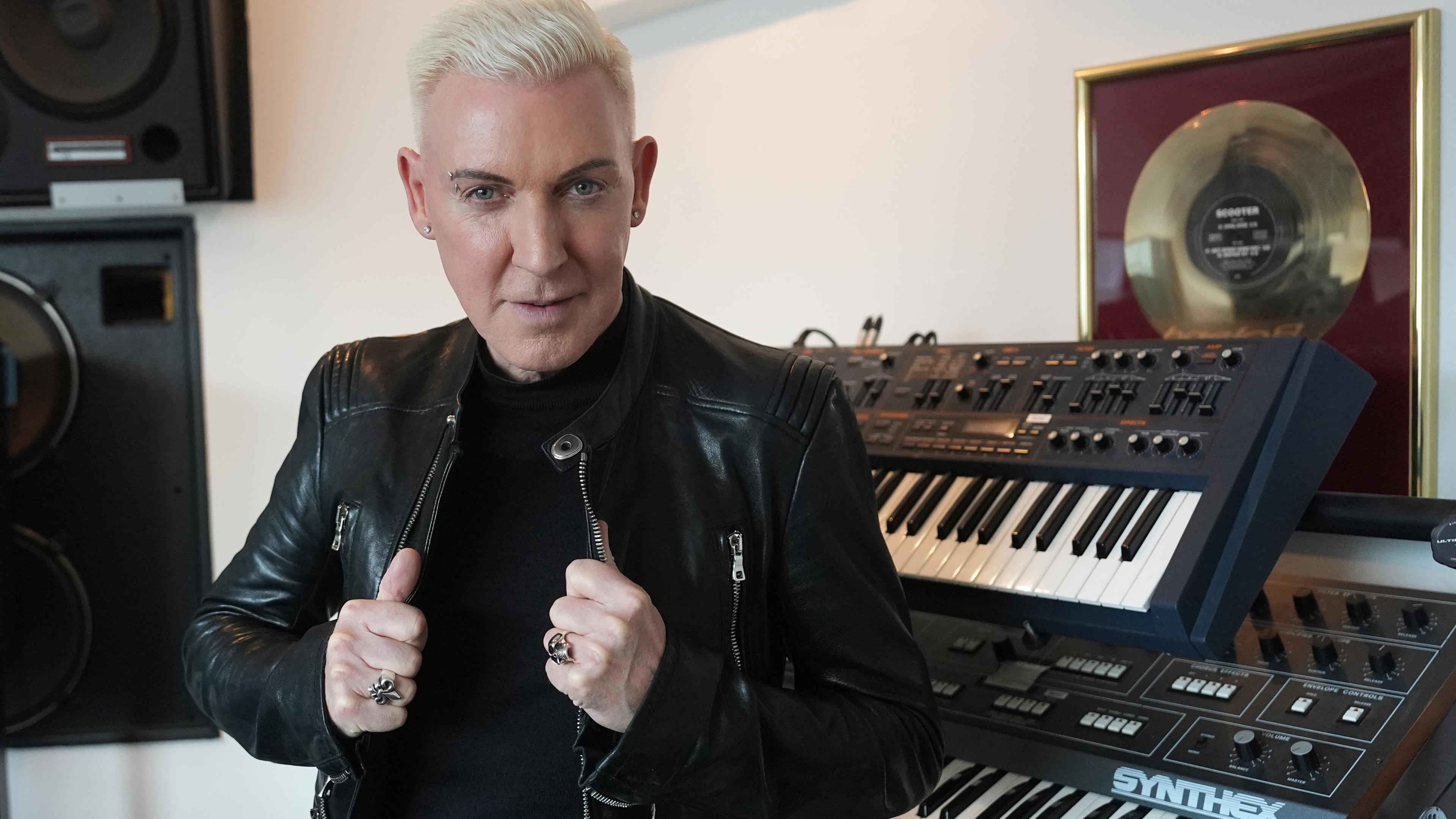 Der Musiker H.P. Baxxter steht in seinem Musikstudio neben Keyboards und der ersten goldenen Schallplatte