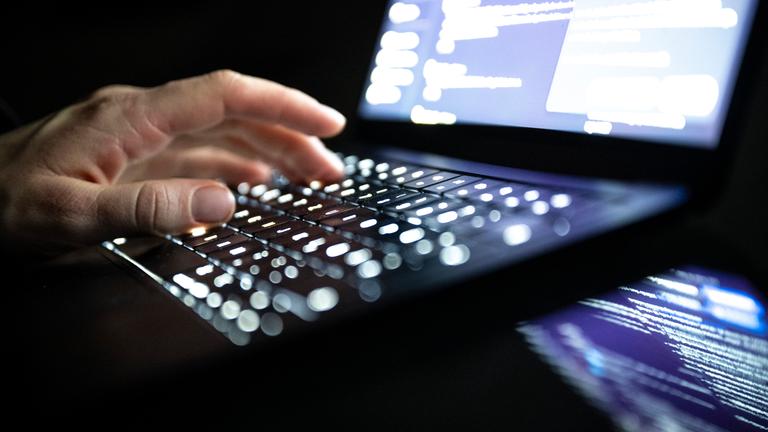 Eine Person tippt mit den Fingern auf einer beleuchteten Laptop-Tastatur.