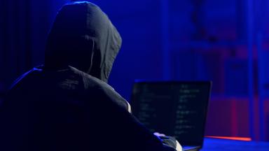 Eine Person mit Kapuze sitzt vor einem Laptop