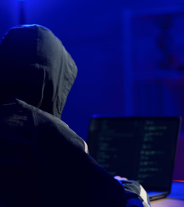 Eine Person mit Kapuze sitzt vor einem Laptop