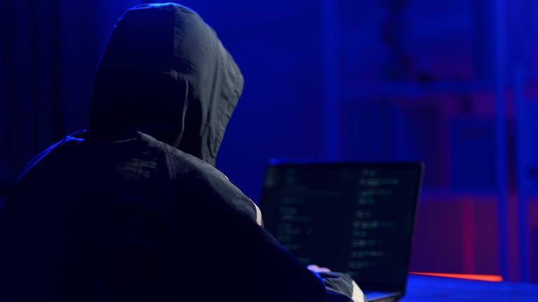 Eine Person mit Kapuze sitzt vor einem Laptop