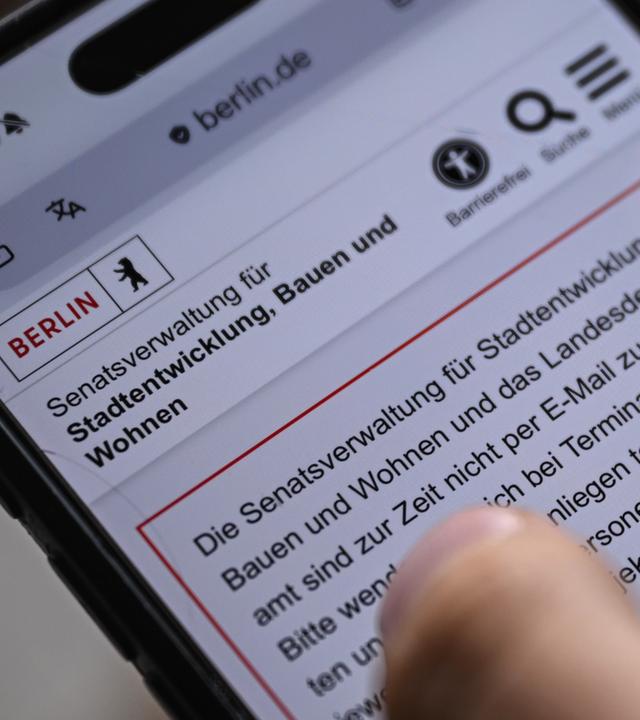 In dieser gestellten Aufnahme hält ein junger Mann ein Smartphone in der Hand, auf dem die Seite der Senatsverwaltung für Stadtentwicklung, Bauen und Wohnen aufmerksam macht, das diese zurzeit nicht erreichbar ist.