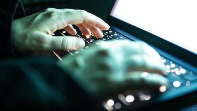 Eine Person tipptmit den Fingern auf einer beleuchteten Tastatur. 