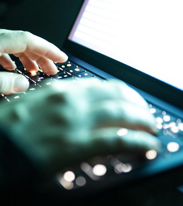 Eine Person tipptmit den Fingern auf einer beleuchteten Tastatur. 