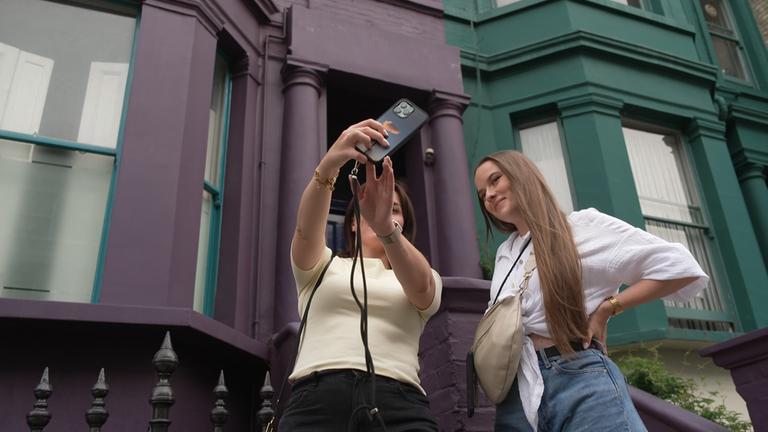 Zwei Mädchen machen ein Selfie vor einem der Häuser