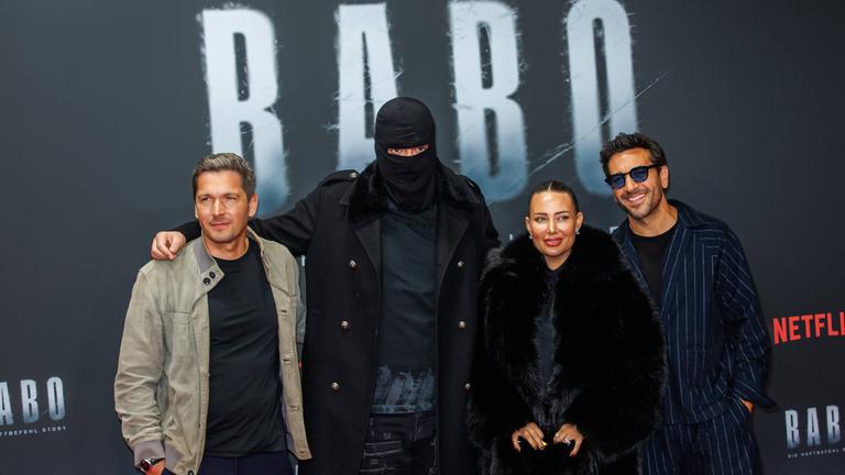 Auf dem Bild ist der Rapper Haftbefehl, seine Ehefrau und die Regiesseure seiner Dokumentation zu sehen. Sie alle posieren auf dem Roten Teppich der Premiere.