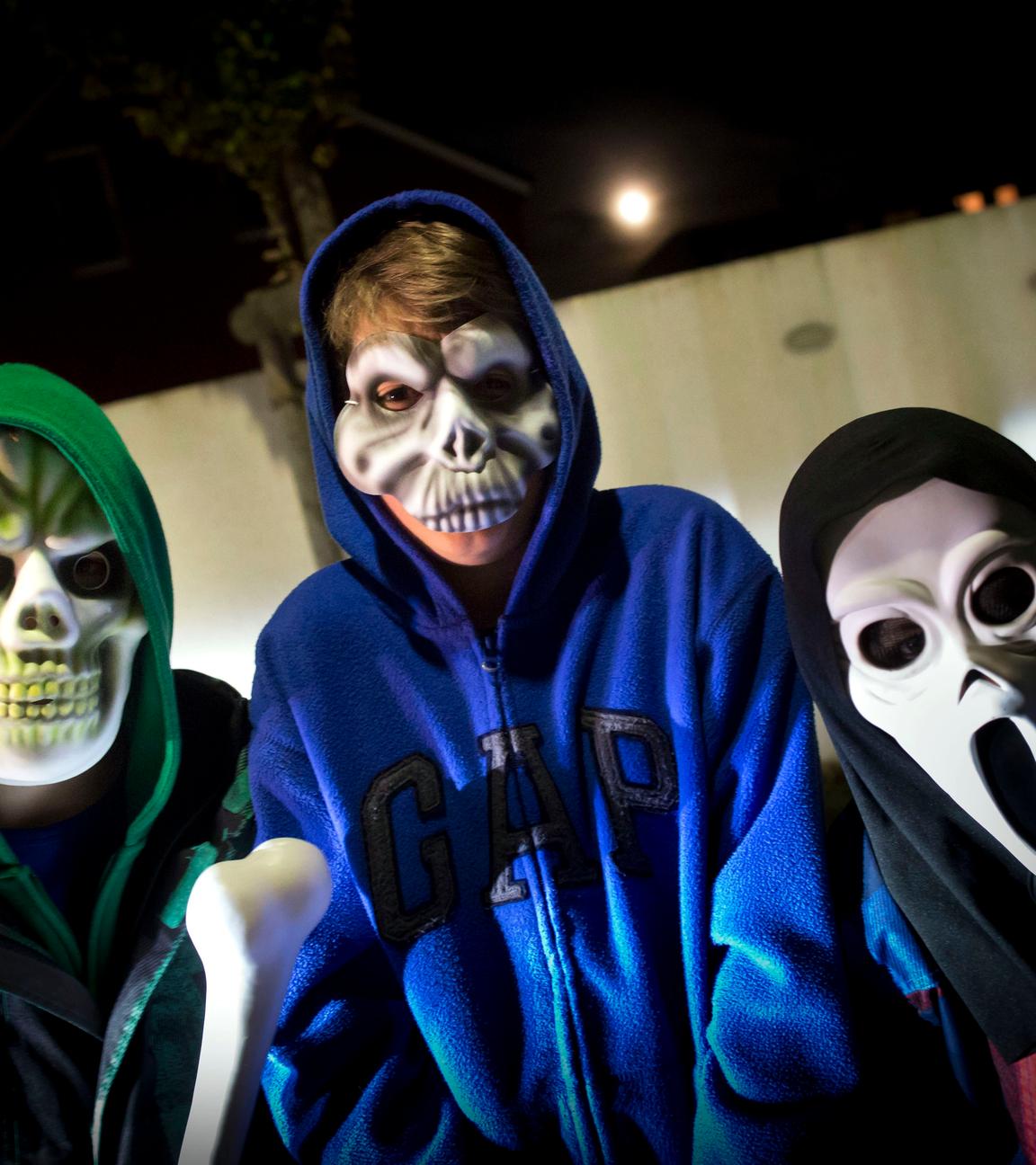 Drei Kinder tragen gruselige Halloween-Masken.