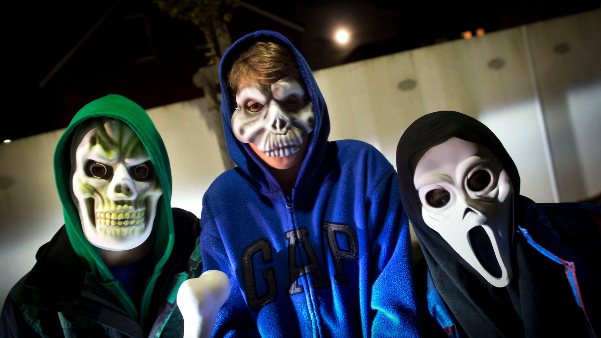 Drei Kinder tragen gruselige Halloween-Masken.