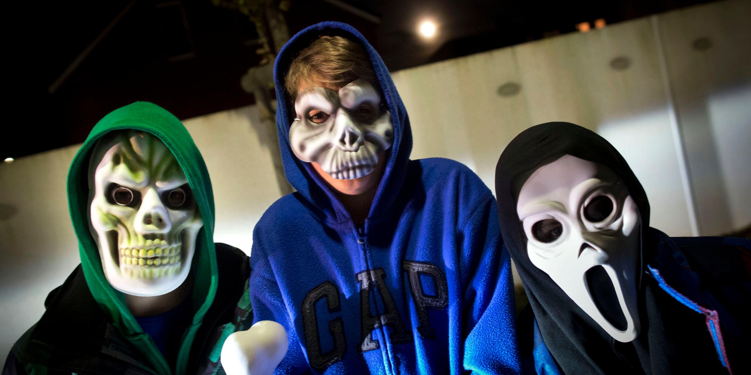 Drei Kinder tragen gruselige Halloween-Masken.