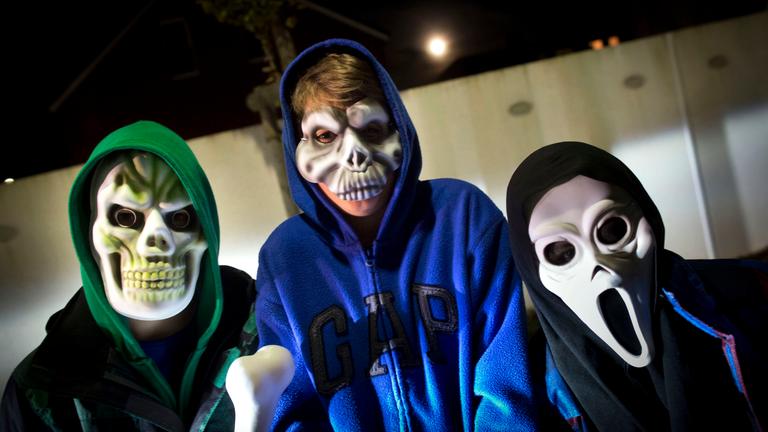 Drei Kinder tragen gruselige Halloween-Masken.
