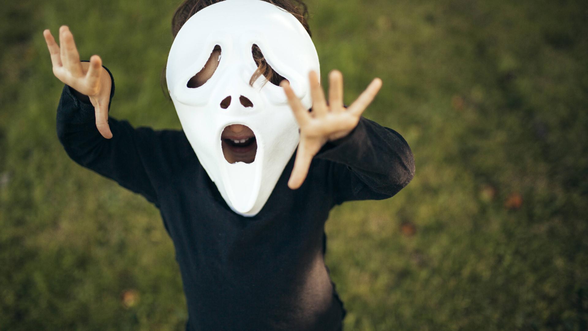 Kind mit schauriger Maske steht auf einer Wiese.