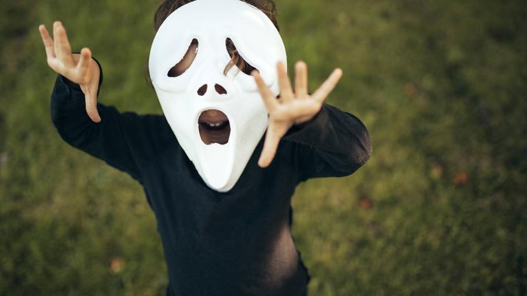 Kind mit schauriger Maske steht auf einer Wiese.