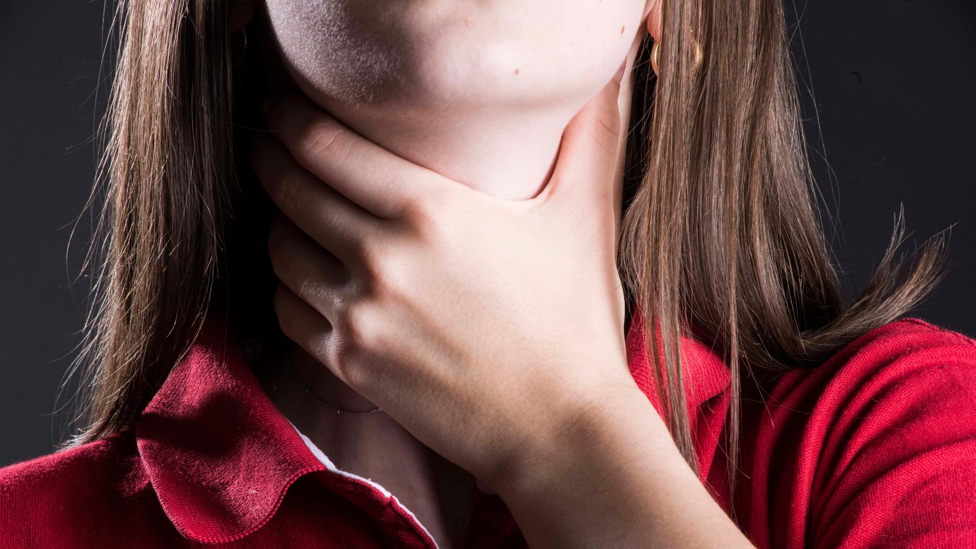 Frau mit Halsschmerzen greift sich an den Hals