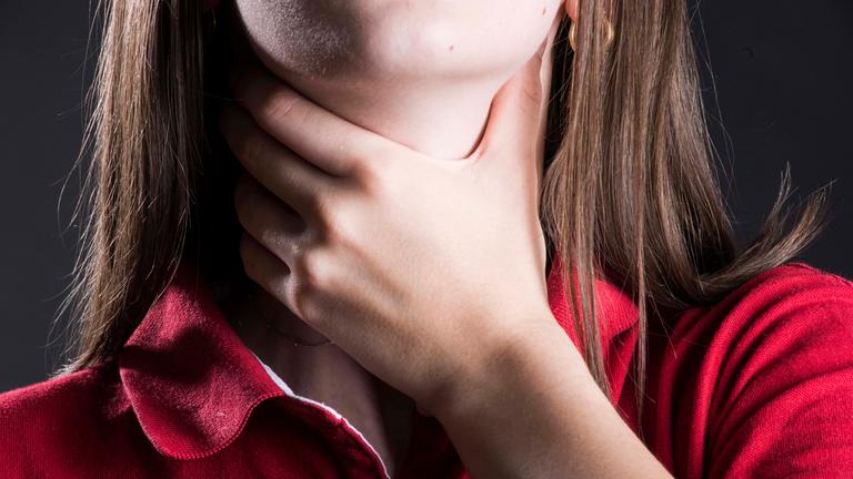 Frau mit Halsschmerzen greift sich an den Hals