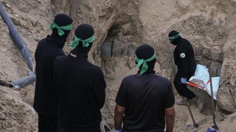 Hamas-Kämpfer tragen einen weißen Sack, vermutlich mit einer Leiche, bei der Suche nach Geisel-Überresten in Hamad City, Süder-Gazastreifen.