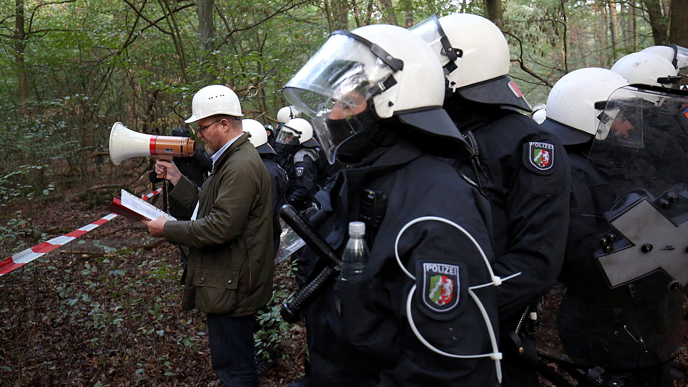 Ein Behördenvertreter kündigt mit einem Megafon die Räumung der Baumhäuser an.