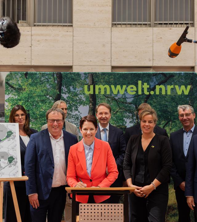 Auf dem Bild sind verschiedene folgende Minister:innen aus NRW zu sehen: Mona Neubaur, Ministerin für Wirtschaft, Industrie, Klimaschutz und Energie (stellvertretende Ministerpräsidentin), Oliver Krischer, Minister für Umwelt, Naturschutz und Verkehr und Silke Gorißen, Landwirtschaftsministerin. Es wird eine Erklärung für den Schutz des Hambacher Waldes unterzeichnet.