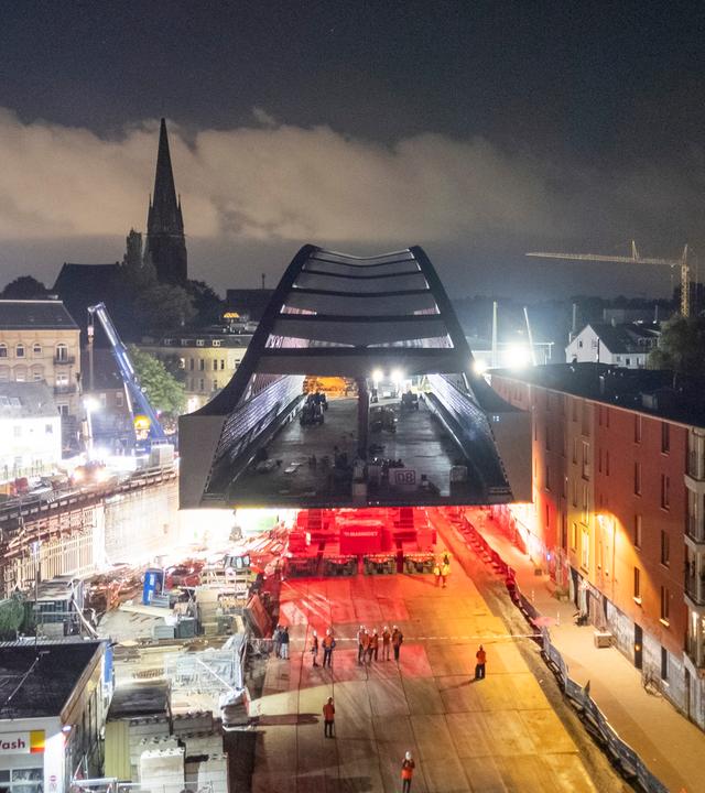 Der Rohbau der neuen Sternbrücke, einer 108 Meter lange und 21 Meter breite, stützenfreie Stabbogenkonstruktion, der auf selbstfahrenden Modultransportern fährt, ist kurz vor dem Ziel. 