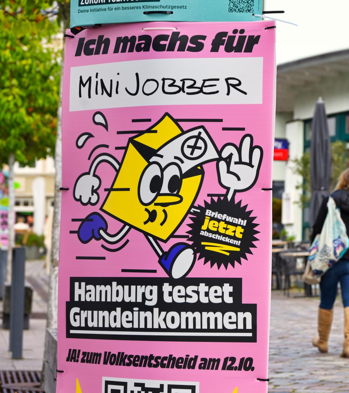 Ein rosa Plakat mit gelbem Briefumschlag wirbt zur Stimmabgabe beim Volksentscheid zum bedingungslosen Grundeinkommen. 