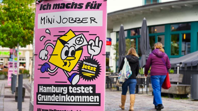 Ein rosa Plakat mit gelbem Briefumschlag wirbt zur Stimmabgabe beim Volksentscheid zum bedingungslosen Grundeinkommen. 